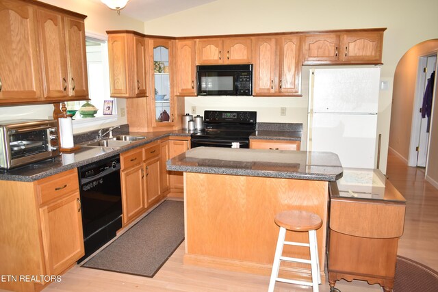 kitchen featuring light wood-type flooring, a center island, black appliances, vaulted ceiling, and sink