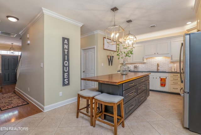 kitchen featuring light tile patterned floors, wood counters, visible vents, and freestanding refrigerator