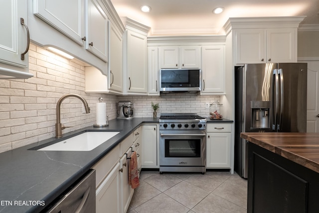 kitchen with light tile patterned floors, stainless steel appliances, a sink, white cabinetry, and decorative backsplash