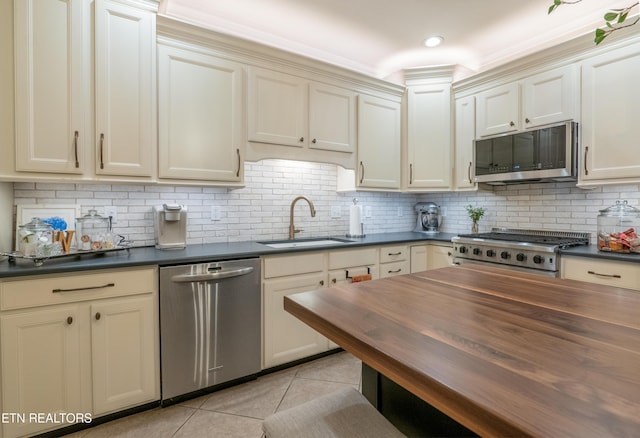 kitchen featuring cream cabinetry, light tile patterned floors, stainless steel appliances, wooden counters, and a sink