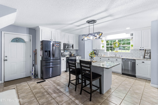 kitchen featuring light tile patterned floors, white cabinets, a kitchen island, light stone countertops, and appliances with stainless steel finishes