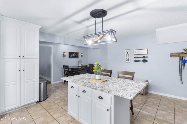 kitchen with light tile patterned flooring, a kitchen island, white cabinets, and decorative light fixtures