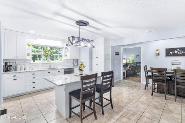 kitchen featuring white cabinets, hanging light fixtures, backsplash, light stone countertops, and a center island