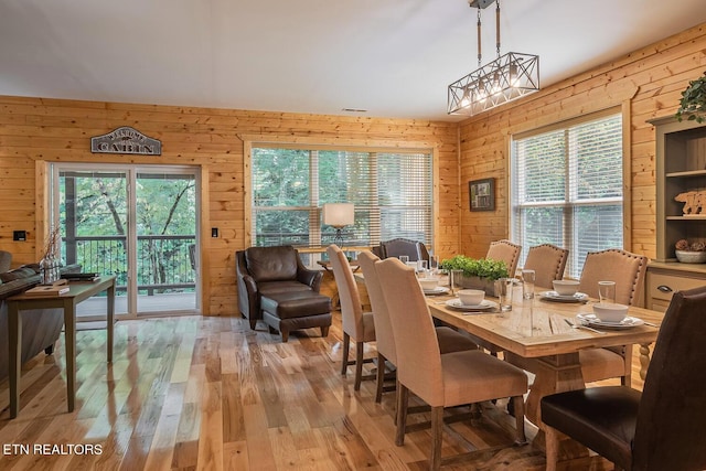 dining room with wood walls, light wood-type flooring, and an inviting chandelier