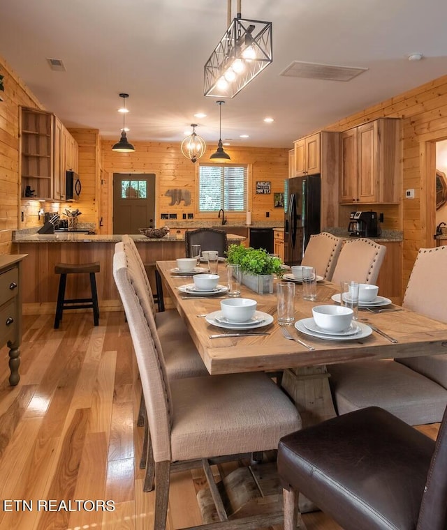 dining area with sink, wooden walls, and light hardwood / wood-style floors