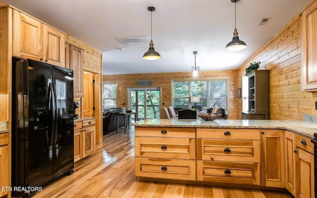 kitchen with black refrigerator with ice dispenser, decorative light fixtures, wood walls, and light hardwood / wood-style flooring