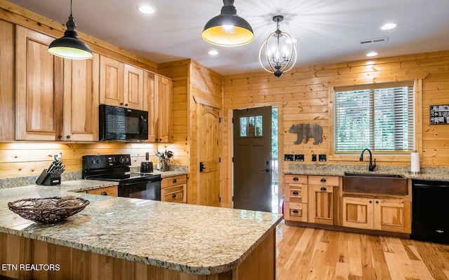 kitchen with wood walls, sink, black appliances, and light hardwood / wood-style floors