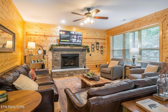 living room with wood walls, a stone fireplace, and ceiling fan