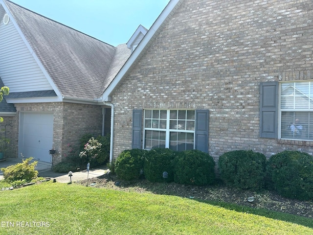 view of property exterior featuring a garage, brick siding, a shingled roof, and a yard