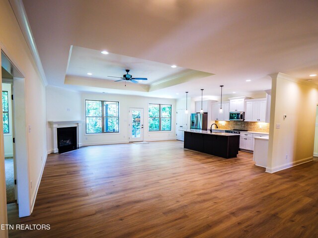 unfurnished living room with a tray ceiling, ceiling fan, hardwood / wood-style flooring, and sink