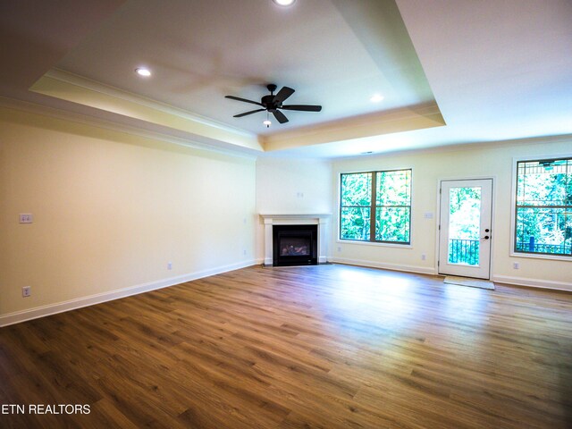 unfurnished living room featuring ceiling fan, crown molding, a tray ceiling, and wood-type flooring