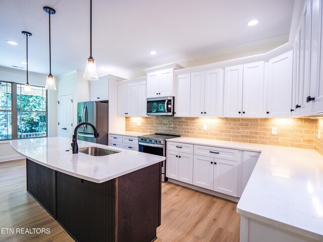 kitchen with decorative backsplash, light hardwood / wood-style flooring, a kitchen island with sink, white cabinetry, and appliances with stainless steel finishes