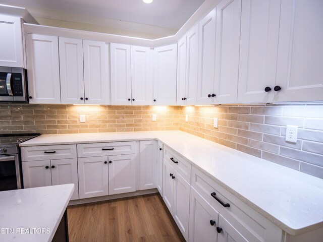 kitchen with white cabinets, decorative backsplash, appliances with stainless steel finishes, and light wood-type flooring