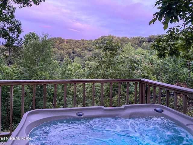 pool at dusk with a deck and a hot tub