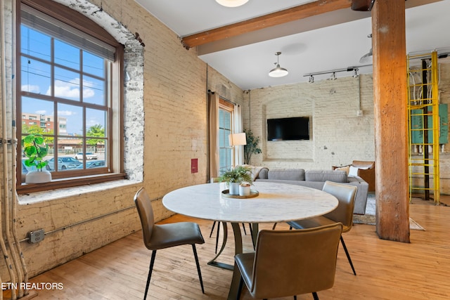 dining space with rail lighting, light hardwood / wood-style floors, beam ceiling, and brick wall