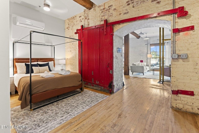 bedroom featuring an AC wall unit, brick wall, and hardwood / wood-style floors