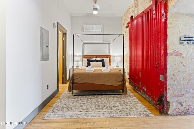 bedroom with electric panel, hardwood / wood-style floors, and an AC wall unit