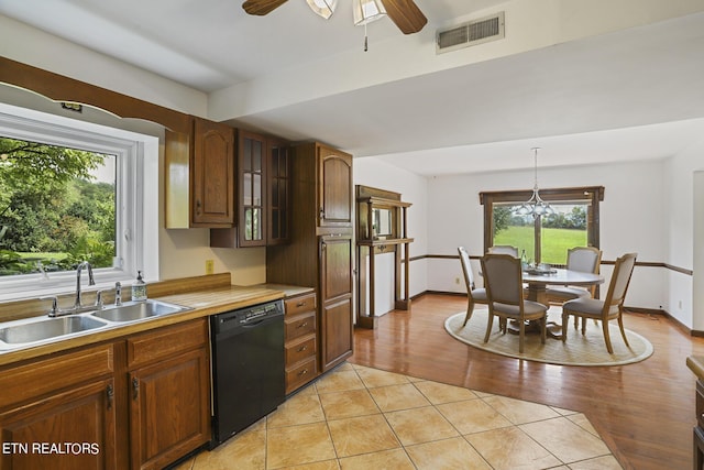 kitchen featuring pendant lighting, sink, light tile patterned floors, black dishwasher, and ceiling fan with notable chandelier