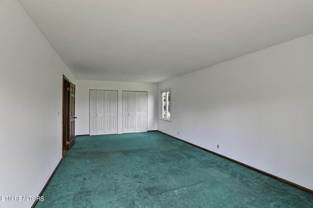 unfurnished bedroom featuring dark colored carpet and multiple closets