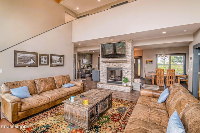 living room with a stone fireplace, a chandelier, wood-type flooring, and a towering ceiling