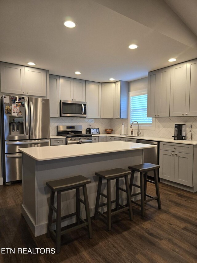 kitchen with gray cabinetry, appliances with stainless steel finishes, dark hardwood / wood-style floors, and a kitchen island