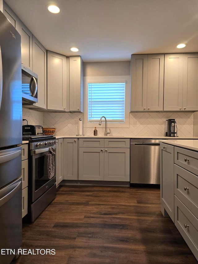 kitchen featuring appliances with stainless steel finishes, dark hardwood / wood-style flooring, gray cabinets, and tasteful backsplash