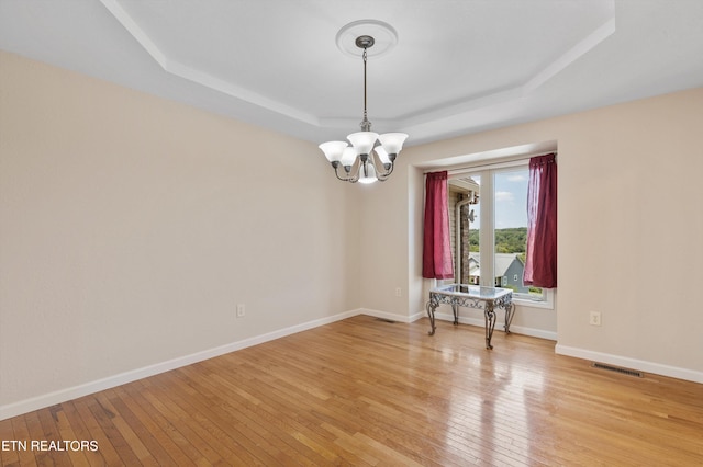 empty room featuring light hardwood / wood-style flooring, an inviting chandelier, and a tray ceiling