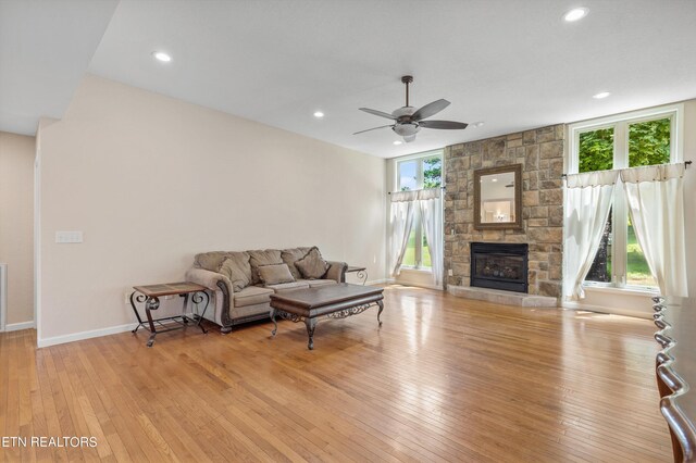 living room with ceiling fan, light wood-type flooring, and a stone fireplace