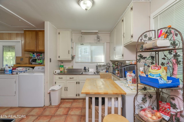 kitchen with light tile patterned floors, white cabinets, independent washer and dryer, a sink, and a wealth of natural light