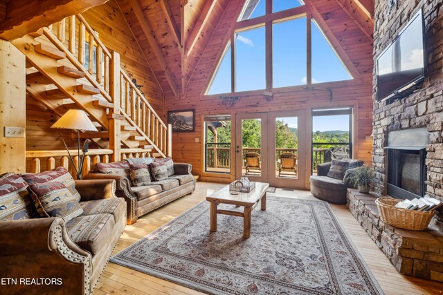 living room featuring wood walls, a fireplace, light wood-type flooring, and high vaulted ceiling