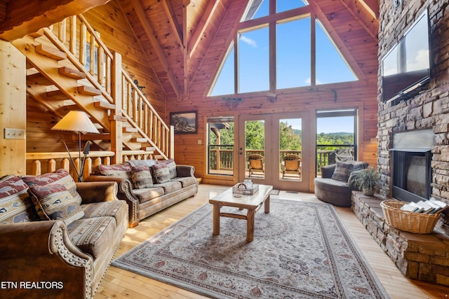 living room with beam ceiling, wooden walls, a stone fireplace, wooden ceiling, and light wood-type flooring