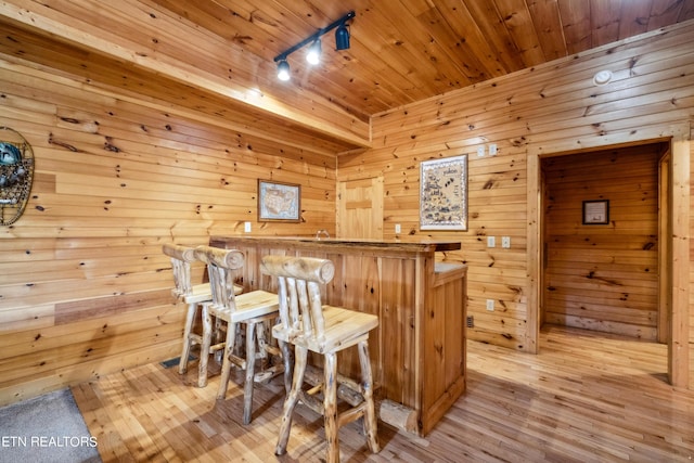 bar with rail lighting, wooden ceiling, light wood-type flooring, and wood walls