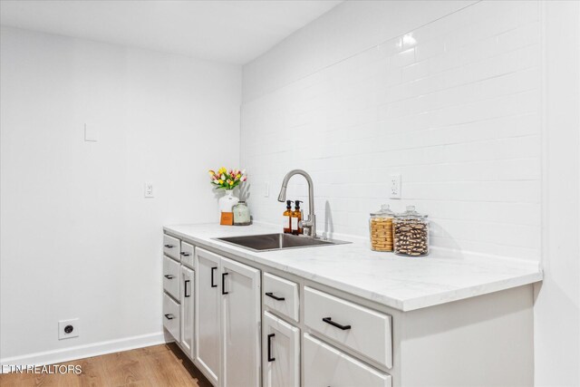 bar featuring light hardwood / wood-style flooring, white cabinetry, sink, and light stone countertops