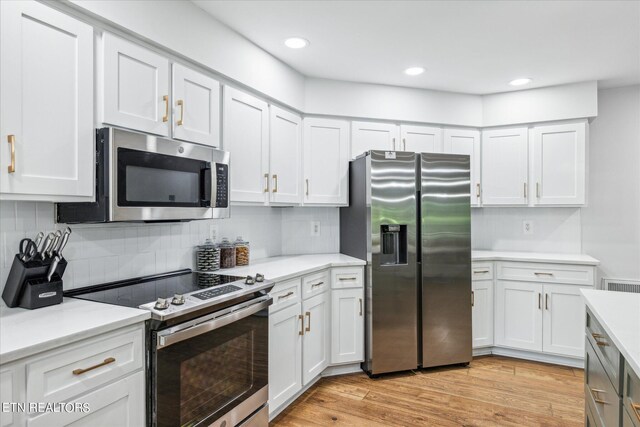 kitchen with tasteful backsplash, white cabinetry, stainless steel appliances, and light hardwood / wood-style floors