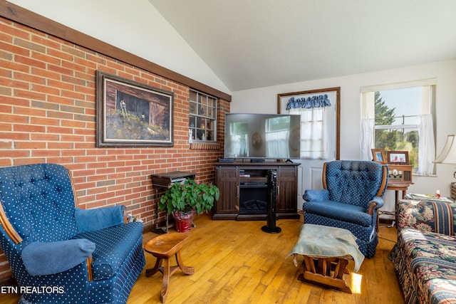 living room with light wood-type flooring, lofted ceiling, and brick wall