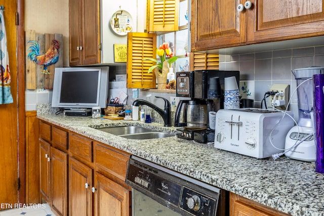 kitchen featuring light stone countertops, dishwasher, sink, and decorative backsplash