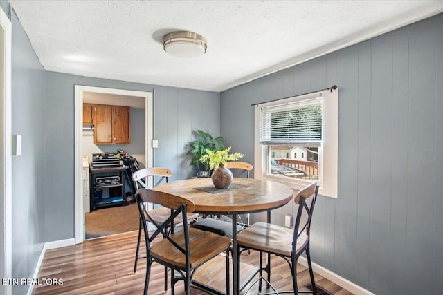 dining area featuring a textured ceiling, light wood-type flooring, and baseboards