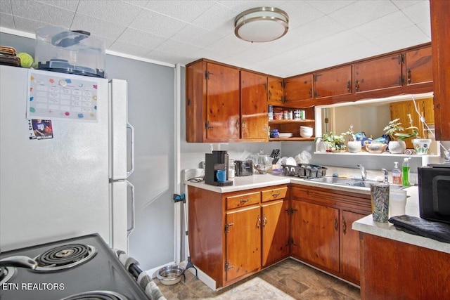 kitchen with light countertops, a sink, freestanding refrigerator, and brown cabinets