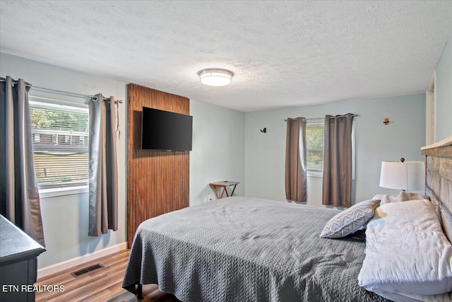 bedroom featuring baseboards, a textured ceiling, visible vents, and wood finished floors