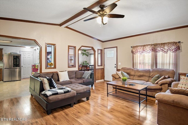 living room with arched walkways, light wood finished floors, lofted ceiling with beams, and ornamental molding