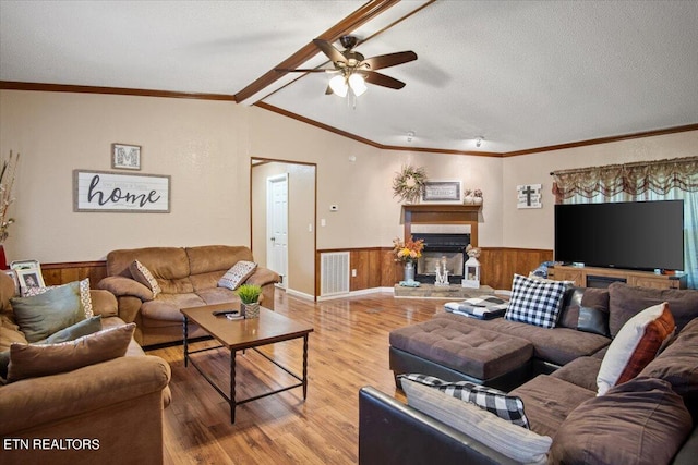 living area with visible vents, a glass covered fireplace, a wainscoted wall, wood finished floors, and a textured ceiling