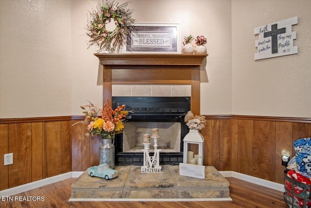 room details with a wainscoted wall, wood finished floors, a tile fireplace, and wooden walls