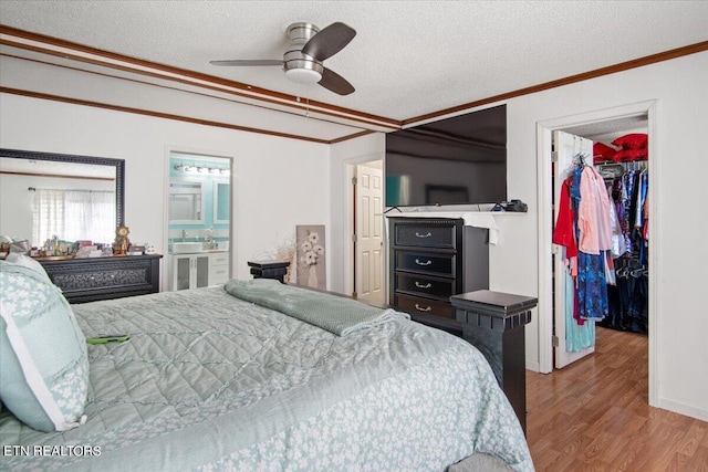 bedroom with a textured ceiling, wood finished floors, a closet, a walk in closet, and crown molding