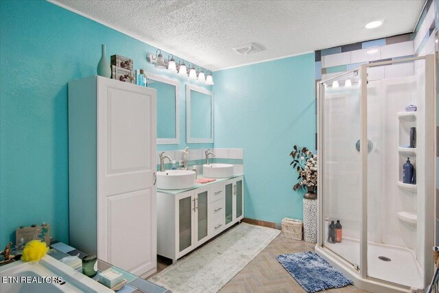 full bathroom featuring a stall shower, a sink, a textured ceiling, and double vanity