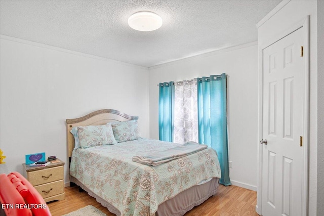 bedroom featuring crown molding, light wood-style flooring, and a textured ceiling