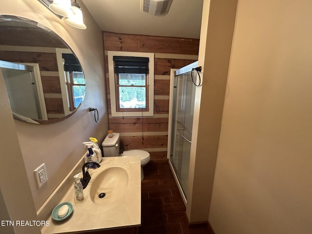 bathroom featuring a shower with shower door, wooden walls, toilet, and vanity