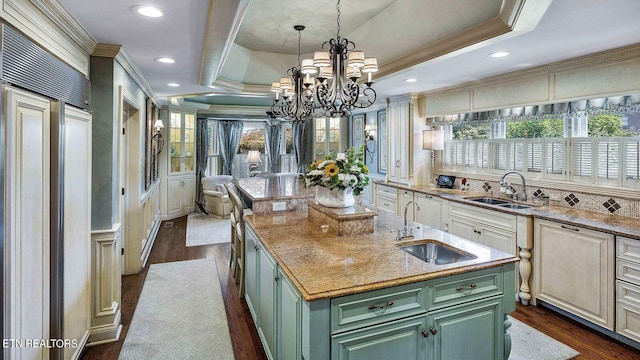 kitchen with dark hardwood / wood-style floors, a kitchen island with sink, a tray ceiling, green cabinetry, and paneled fridge