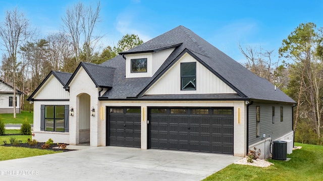 modern inspired farmhouse featuring a front lawn, a garage, central air condition unit, brick siding, and a shingled roof