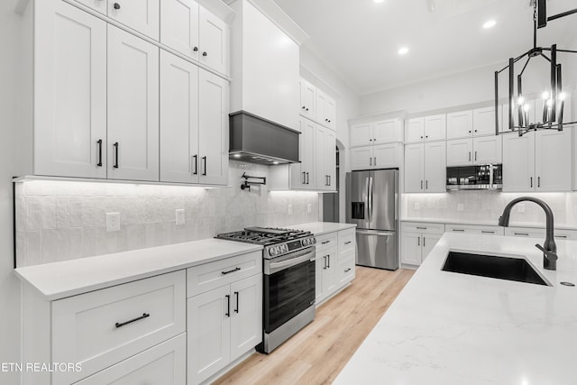 kitchen featuring stainless steel appliances, pendant lighting, light wood-style floors, white cabinetry, and a sink