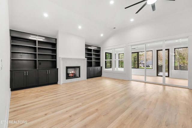 unfurnished living room featuring a warm lit fireplace, light wood finished floors, vaulted ceiling, and plenty of natural light